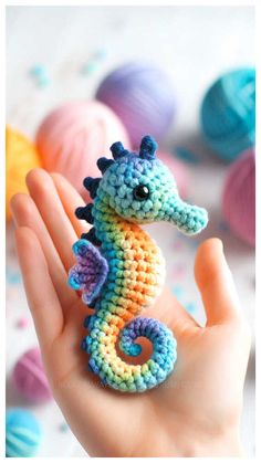 a hand holding a small crocheted seahorse in front of balls of yarn