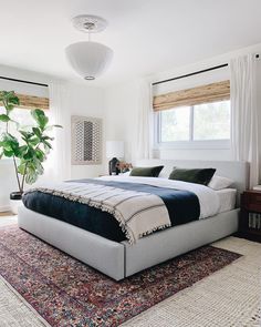 a bedroom with a large bed and rugs on the floor in front of two windows