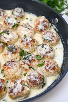 a pan filled with meatballs covered in white sauce and garnished with parsley