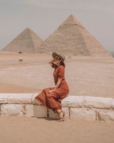 a woman in a red dress and hat sitting on a wall near the pyramids