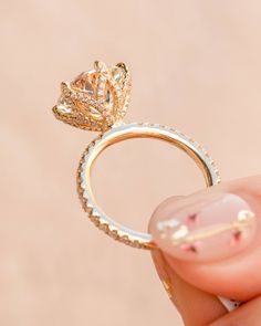 a woman's hand holding a gold ring with a flower design on the side