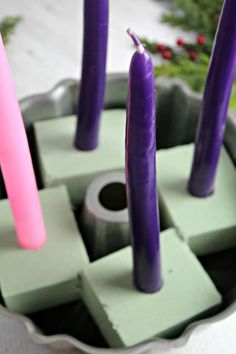 purple candles are in a metal container with green blocks and pink sticks sticking out of them