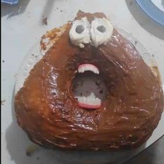 a chocolate frosted doughnut with googly eyes and mouth wide open on a plate