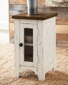 a white cabinet sitting on top of a rug next to a wooden table with a vase