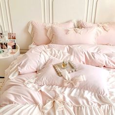 a bed with pink comforters and pillows on it in a white room next to a table