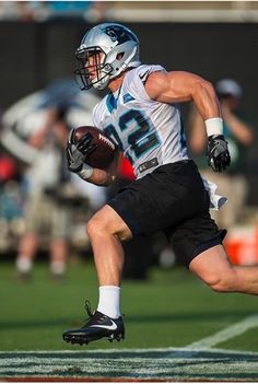 a football player running with the ball in his hand and wearing black shorts, white shirt and helmet