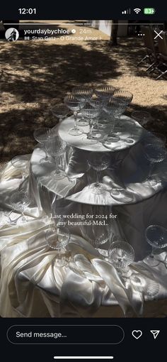 the table is covered with white cloths and glassware for an outdoor wedding reception