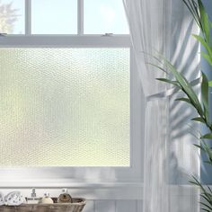 a bathroom window with white curtains and green plants