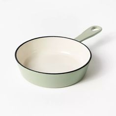 a white and green frying pan on a white surface with a black stripe around the rim