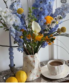 a vase filled with blue and yellow flowers next to a cup of coffee on a table