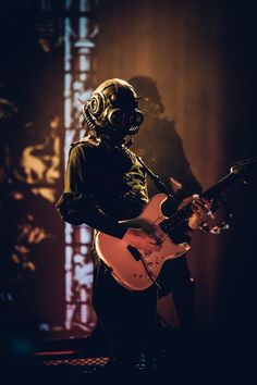 a man in gas mask playing an electric guitar on stage with his headphones on