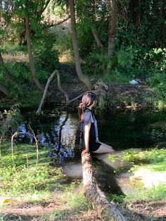 a woman sitting on top of a log in the middle of a forest next to a river