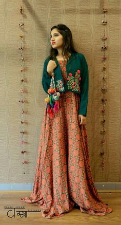 a woman standing in front of a wall wearing an orange and blue dress with flowers on it