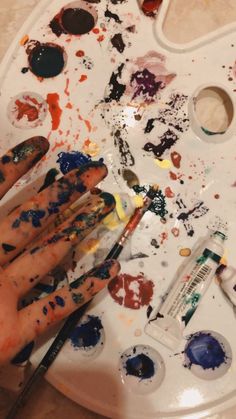 someone's hand with paint and brushes on top of a white tray filled with paints