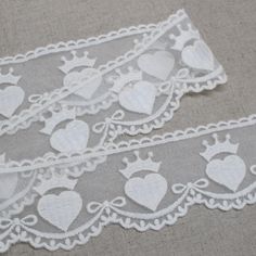 two pieces of white lace with hearts and crowns on the edge are laying next to each other