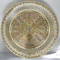 a decorative gold plate with intricate designs on it's sides and center, sitting on a white surface