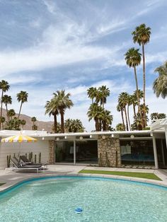 an outdoor swimming pool surrounded by palm trees and lounge chairs in front of a house