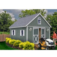 a man standing next to a lawn mower in front of a small gray shed