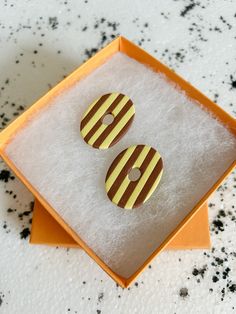 two yellow and brown striped buttons in a box