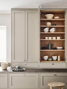 an open cabinet in the middle of a kitchen filled with white dishes and mugs