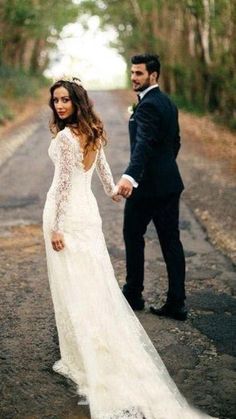 a bride and groom holding hands while walking down the road in their wedding dress with long sleeves