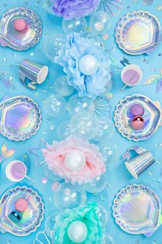 there are balloons, plates and other decorations on this blue tablecloth with pastel colors