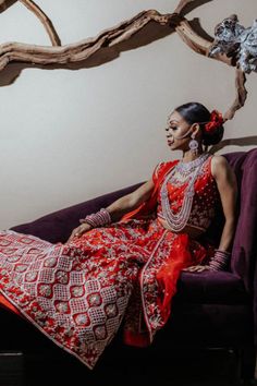 a woman sitting on top of a purple couch wearing a red and white dress with intricate designs