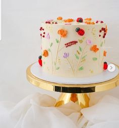 a white cake with flowers and ladybugs on it sitting on a gold stand