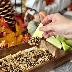 a person is picking up some food from a wooden tray with apples and other autumn decorations