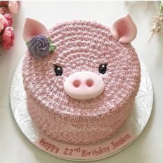 a pink birthday cake with a pig face on it's side and flowers in the background