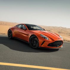 an orange sports car is driving down the road in the middle of the desert with sand dunes behind it