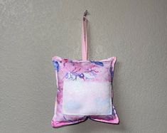 a pink and white pillow hanging on a wall with a hook in the corner that has flowers painted on it