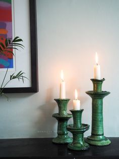 three candles are lit on a table in front of a painting