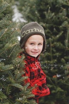 a young boy wearing a red and black plaid shirt standing in front of a christmas tree