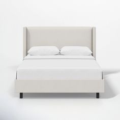 a bed with white sheets and pillows on it's headboard, in front of a wall