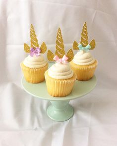 three cupcakes on a cake plate decorated with gold glitter bows and unicorn ears