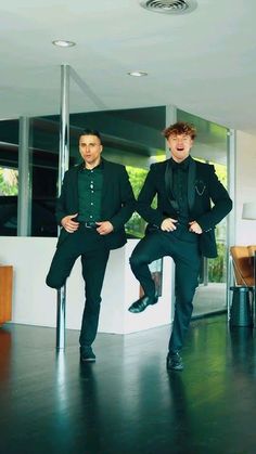 two young men in suits are posing for a photo inside an apartment with wood flooring