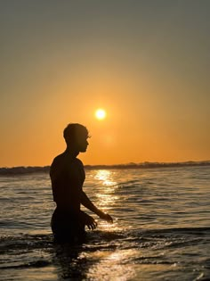 a man wading in the ocean at sunset