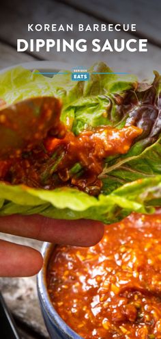 a hand holding a lettuce filled with dipping sauce next to a bowl of chili