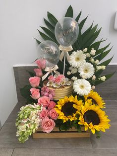 an arrangement of sunflowers, roses, and balloons in a wooden box on a table