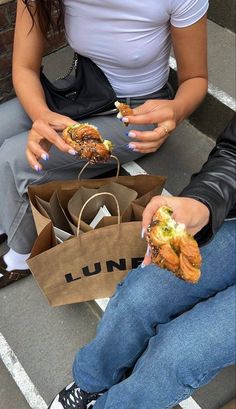 two people sitting on the ground eating sandwiches