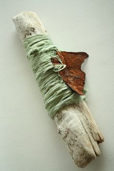 a piece of drift wood with a butterfly on it's back and green fabric wrapped around the ends