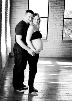 a pregnant couple is posing for a black and white photo in an empty room with large windows