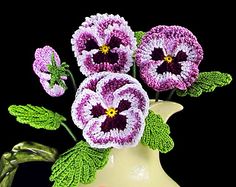 crocheted flowers in a white vase with green leaves