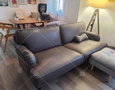 a couch and ottoman in a room with wood flooring next to a table, chair and lamp