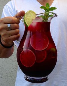 a man is holding a red pitcher filled with liquid and garnished with lime