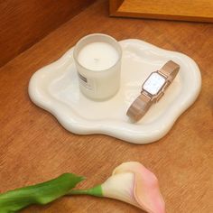 a candle, watch and flower on a tray with a glass of water next to it