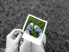 a person holding up a polaroid with their feet in the grass