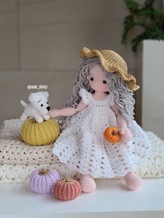 a crocheted doll holding a pumpkin next to two stuffed animals on a white blanket