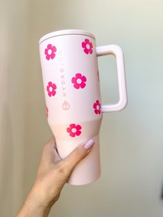 a hand holding a pink and white coffee cup with flowers painted on the side,